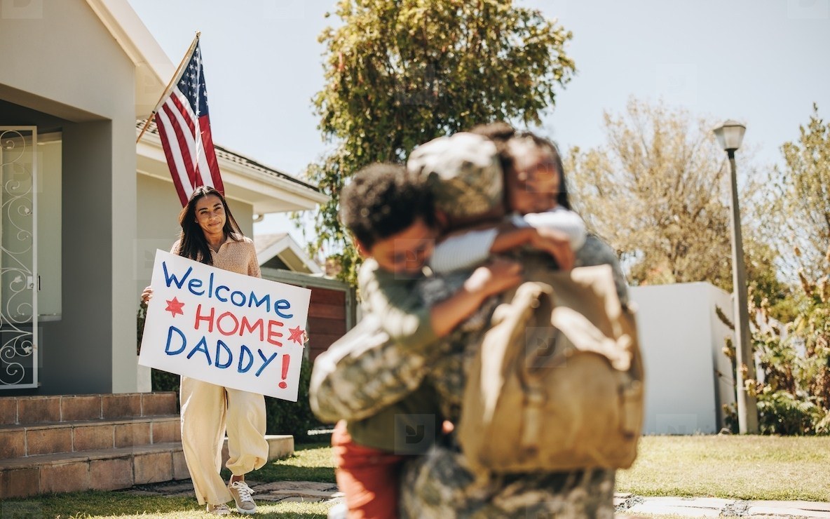 Soldier in uniform hugged by child with Welcome Home Daddy sign
